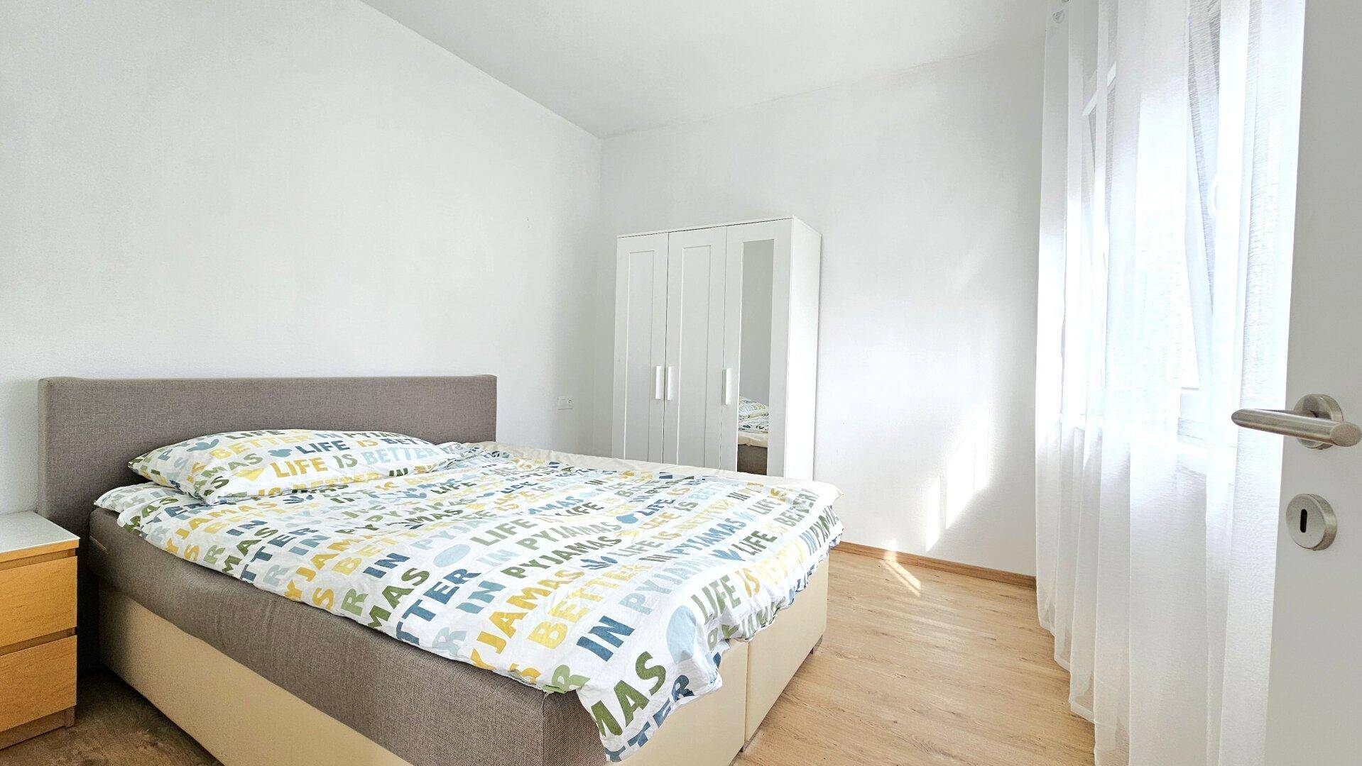 Helles Schlafzimmer mit Doppelbett, Holzboden und weißem Kleiderschrank.