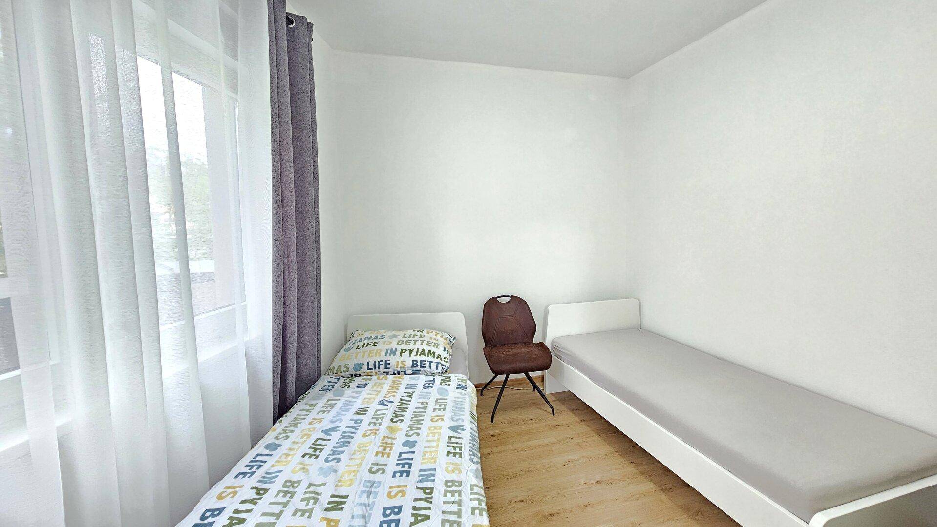 Schlafzimmer mit zwei Einzelbetten, Holzboden und hellen Vorhängen.