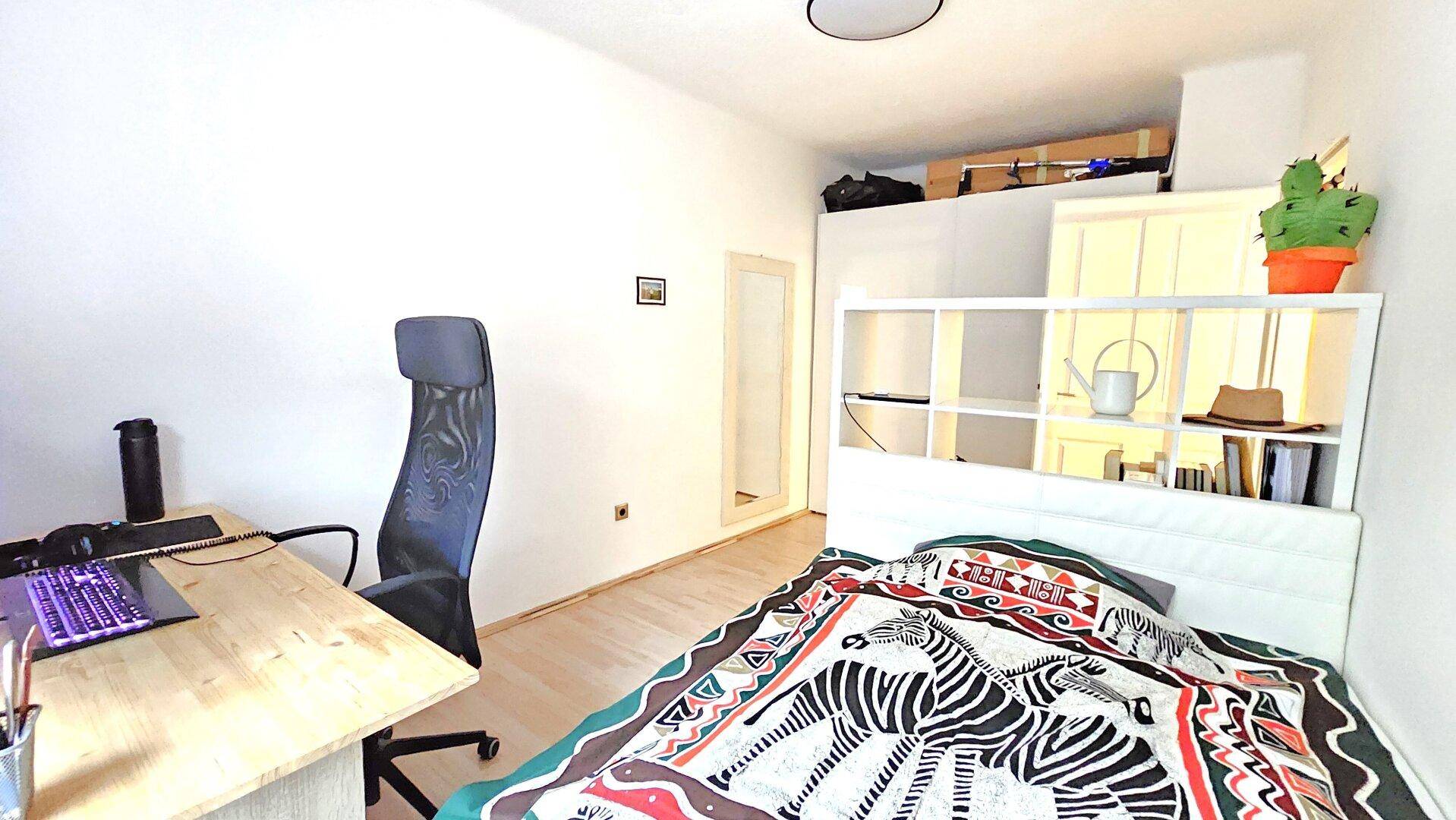 Helles Schlafzimmer mit Arbeitsbereich, Bett und praktischem Regal als Raumteiler.
