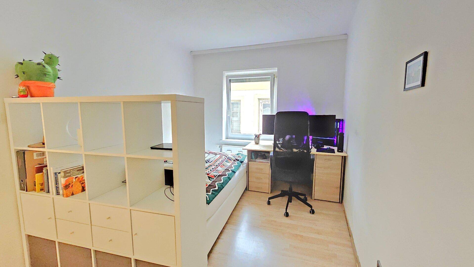 Modern eingerichtetes Schlafzimmer mit Schreibtisch, Computermonitoren und Fenster.