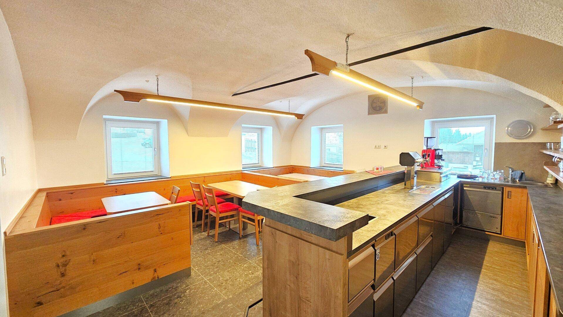 Gemütlicher Essbereich mit Holzbänken, Tischen und einer Bar unter einem Gewölbedach.