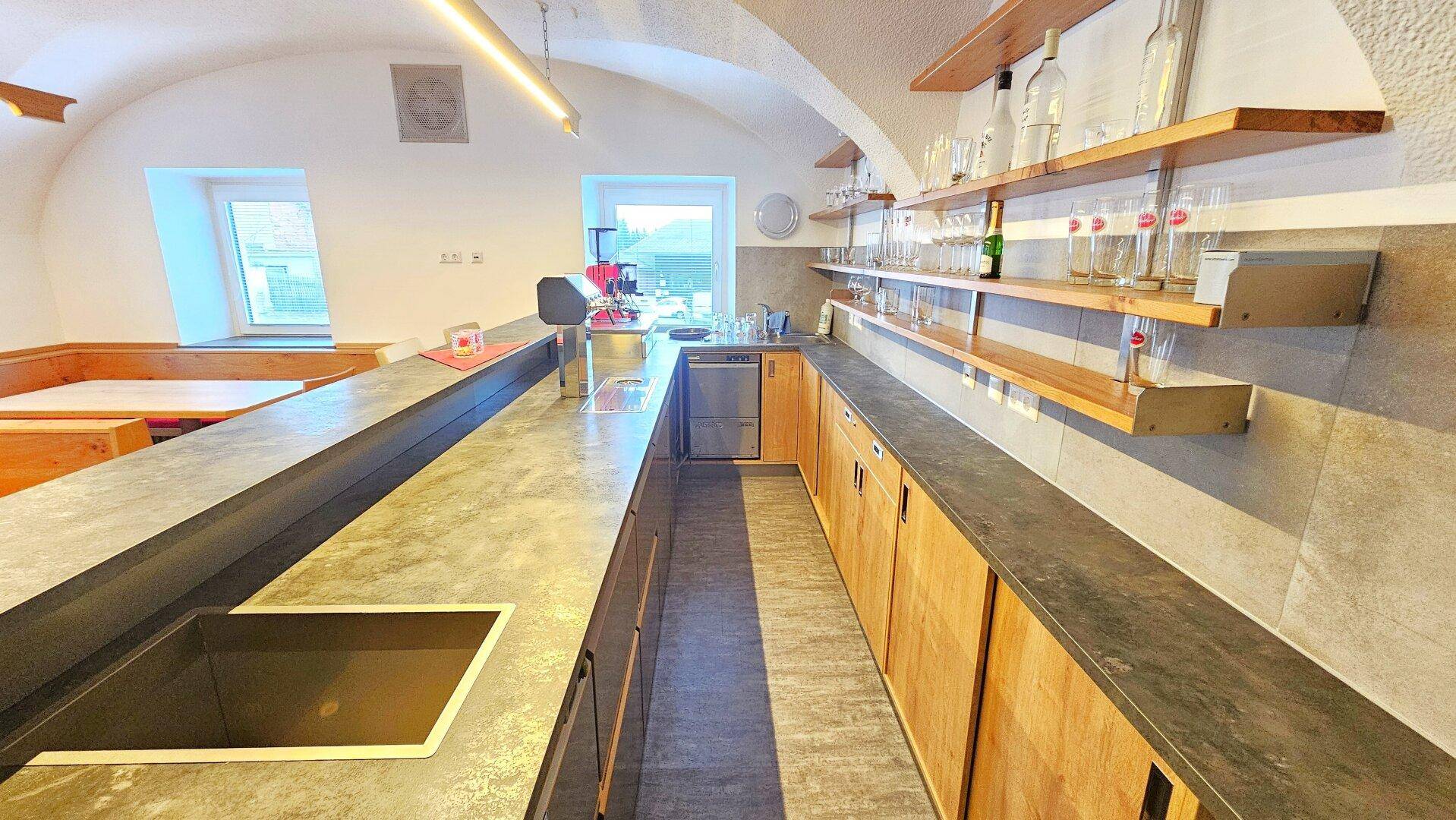 Moderne Küchenzeile mit Theke, Spülbecken und integrierten Geräten unter einem Gewölbedach.