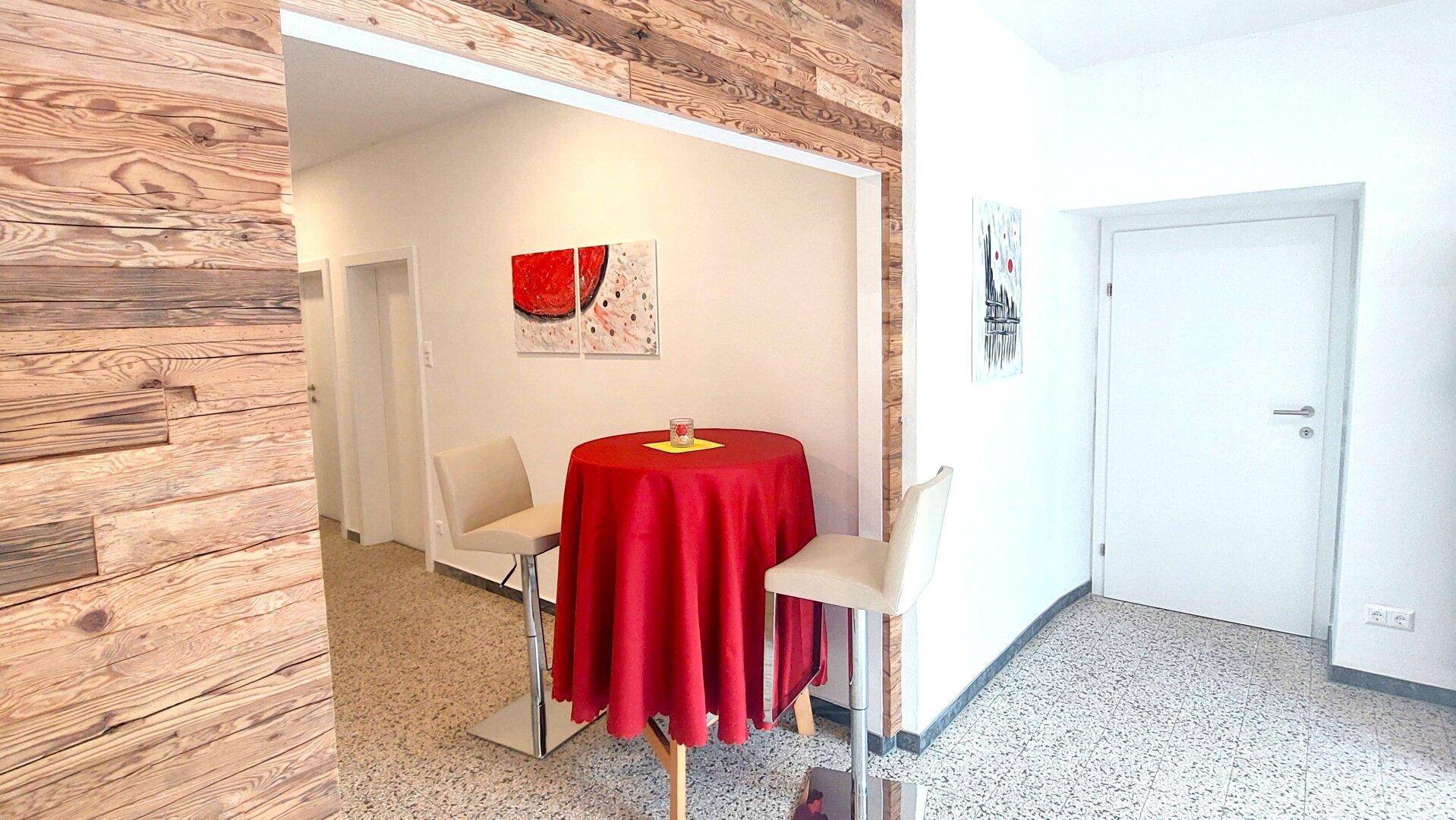 Eingangsbereich mit Holzwandverkleidung, kleinem Stehtisch und moderner Kunst an der Wand.