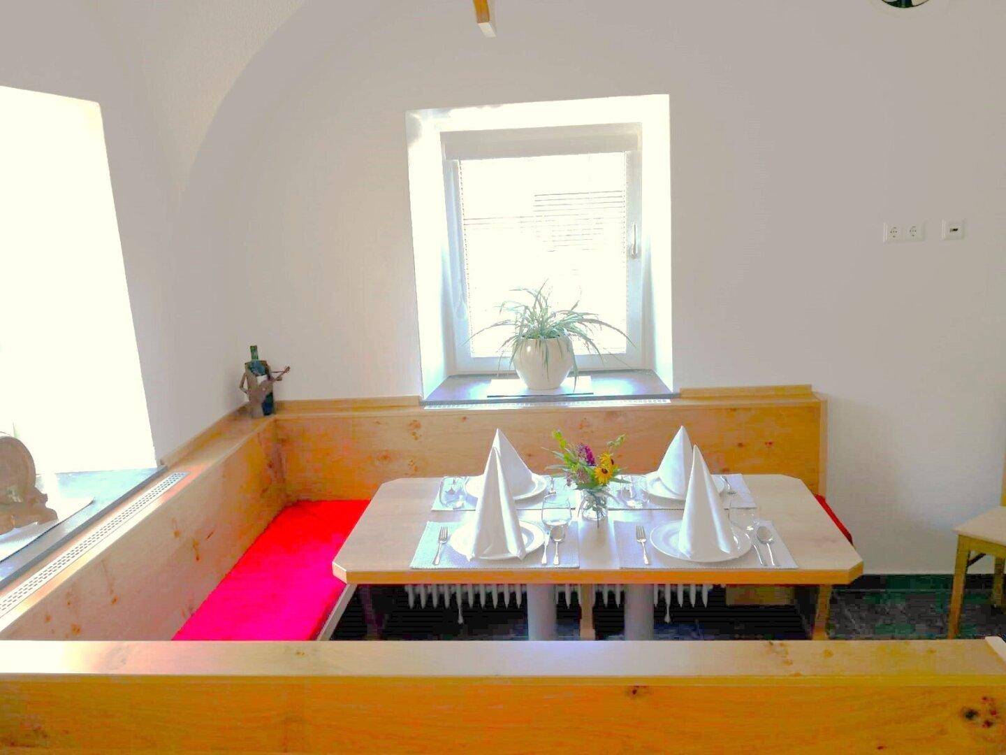 Ein gedeckter Tisch in einem hellen Essbereich mit Holzbänken und einem Fenster.