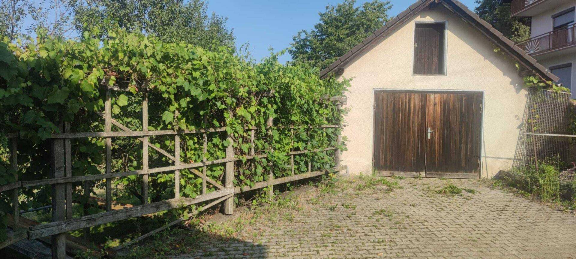 Rustikale Garage mit Holztoren und einer begrünten Pergola, die den Eingangsbereich schmückt.