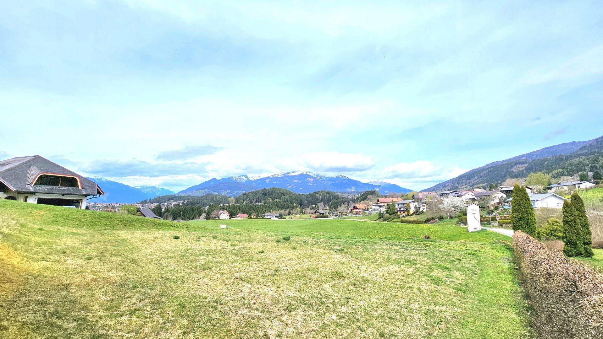 Offenes Feld mit Blick auf eine ländliche Siedlung und die majestätischen Berge am Horizont.