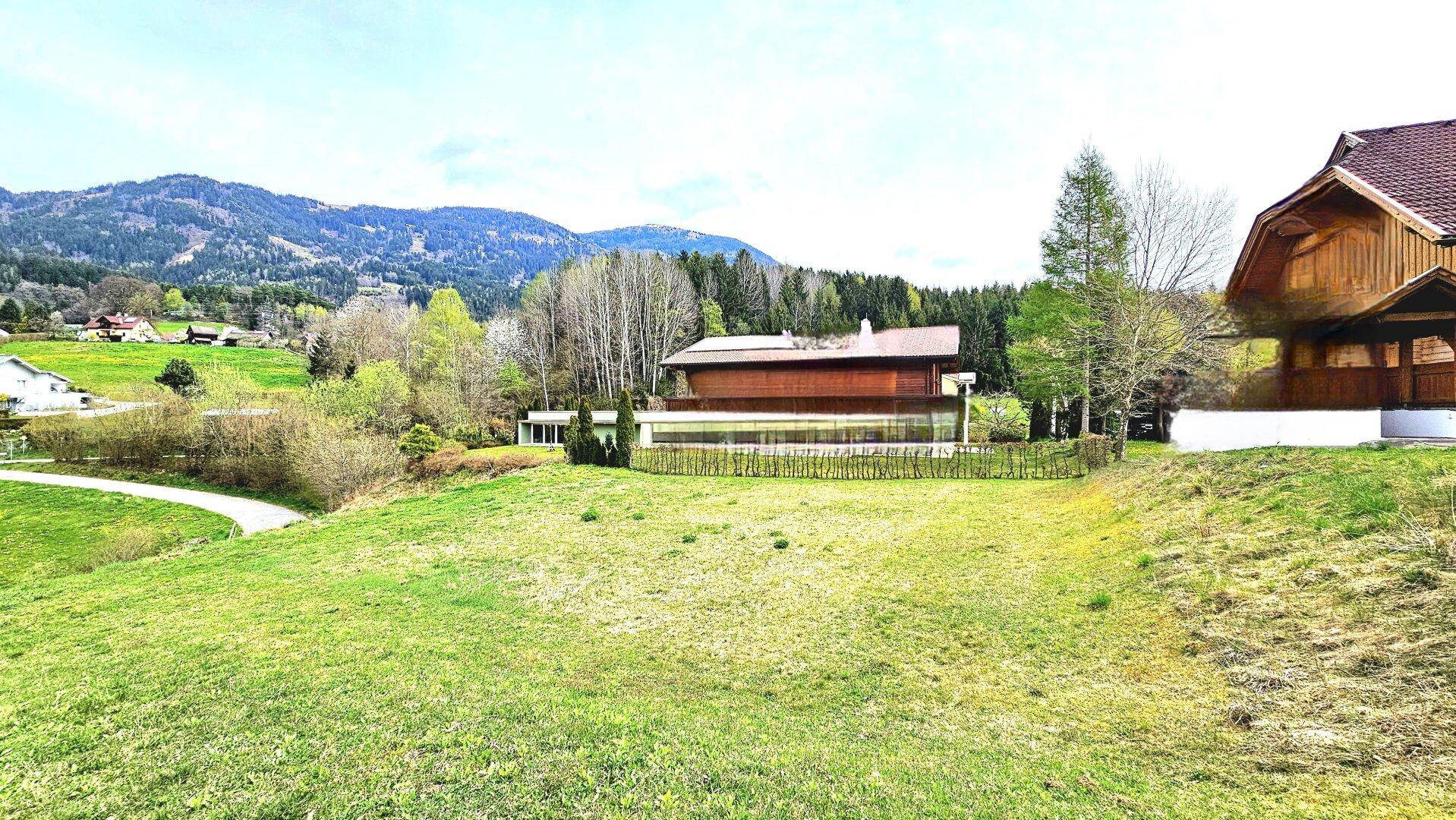 Weitläufiges grünes Grundstück mit Blick auf ein modernes Haus und bewaldete Hügel in der Ferne.