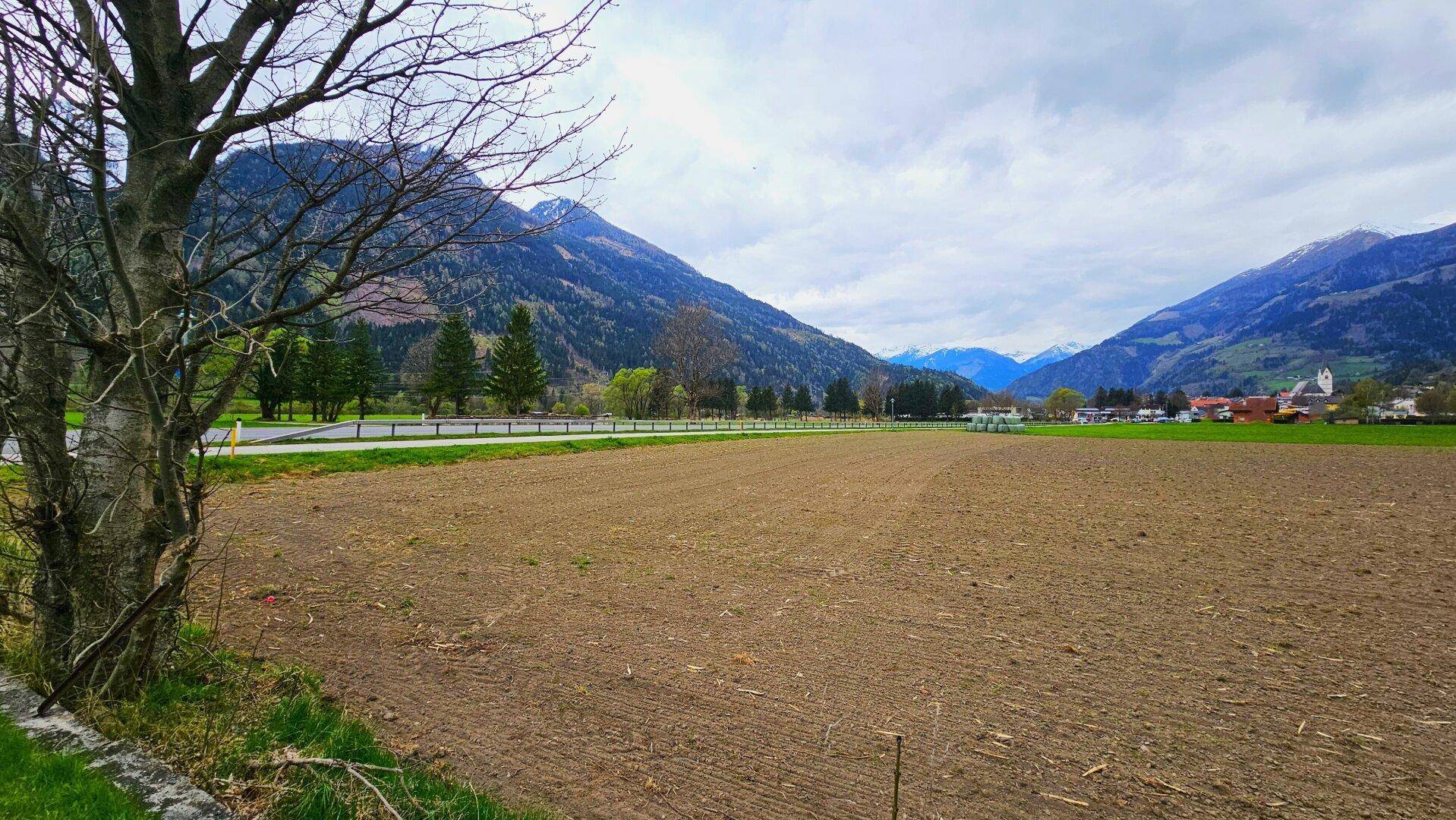 Blick über ein weites Feld auf die majestätische Bergkette und ein idyllisches Dorf am Horizont.