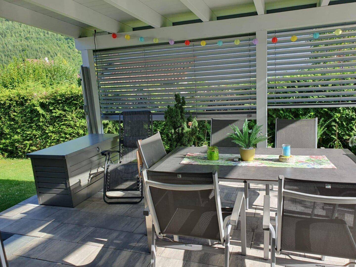 Gemütliche überdachte Terrasse mit Esstisch, Stühlen und dekorativer Beleuchtung.