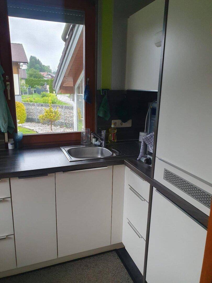 Kompakte Küche mit weißer Einbauküche, Spüle und Fenster mit Gartenblick.