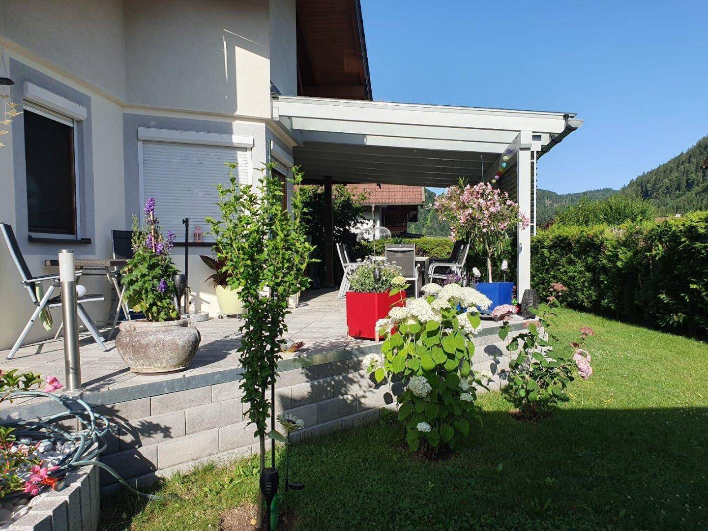 Sonnige Gartenseite des Hauses mit blühenden Pflanzen und Zugang zur Terrasse.