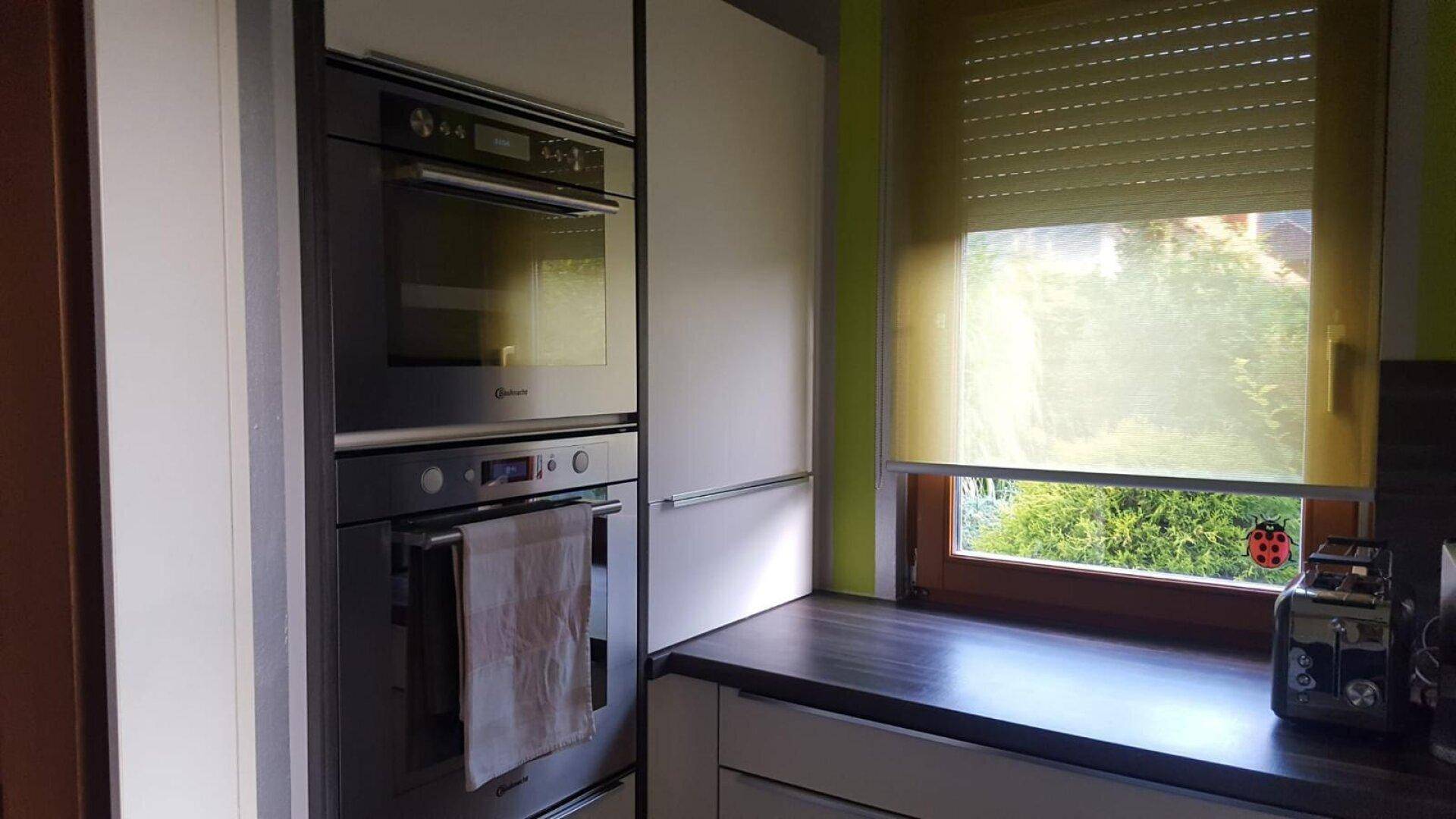Küchenzeile mit Einbaugeräten, Fenster und Rollladen für Privatsphäre.