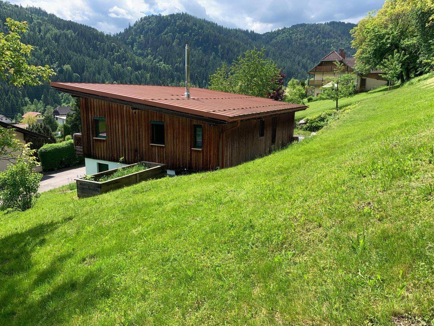 Das Holzhaus mit rotem Dach, eingebettet in die grüne, hügelige Landschaft.