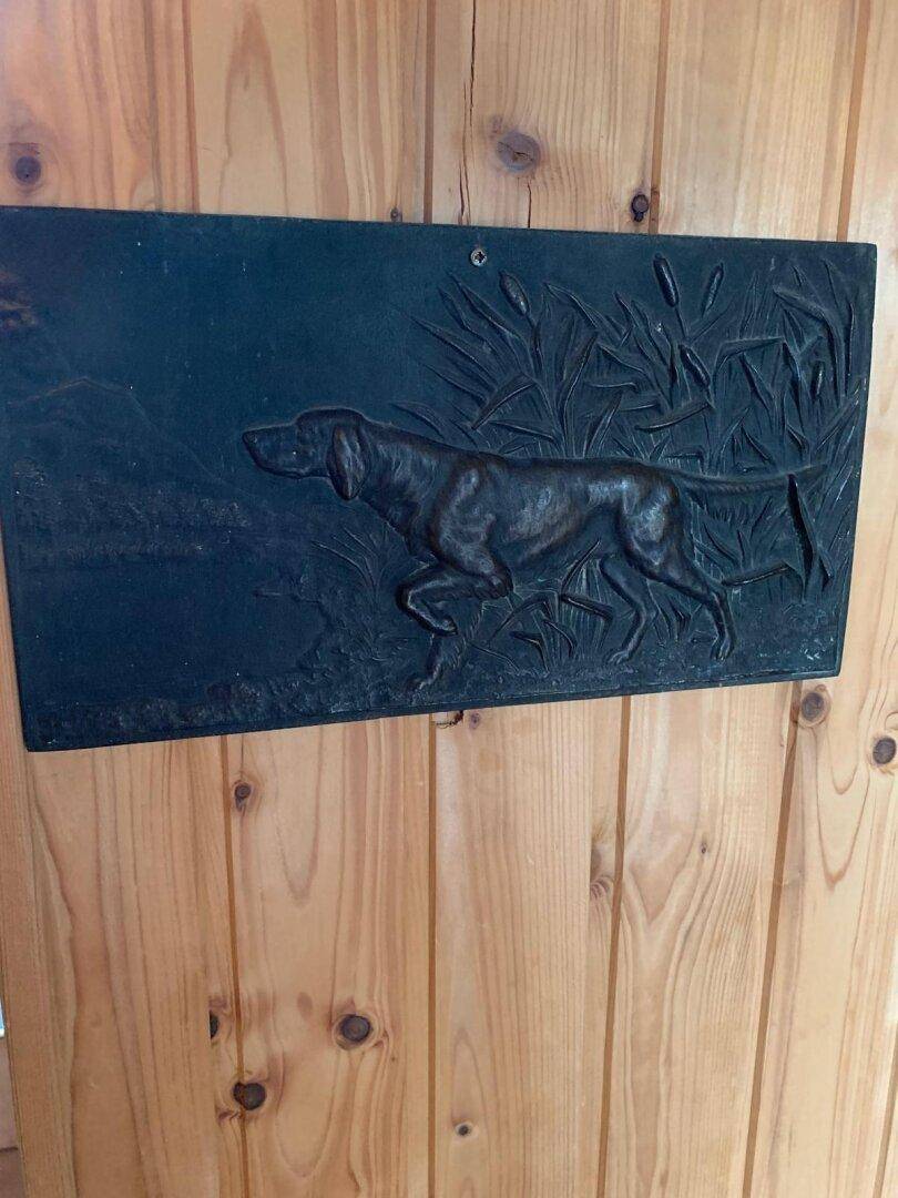 Dekorative Wandtafel mit Jagdhundmotiv an einer rustikalen Holzwand.