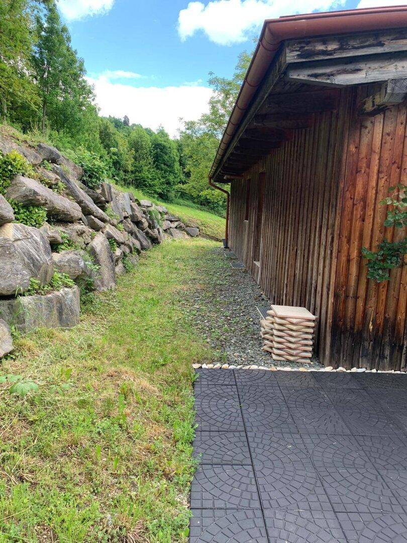 Seitenansicht des Hauses mit Holzfassade, angrenzender Felswand und schmalem Weg.