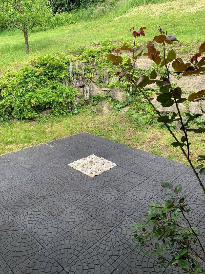 Gepflasterter Außenbereich mit dekorativem Steinmuster, umgeben von Rasen und Pflanzen.