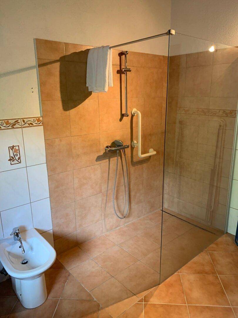 Badezimmer mit begehbarer Dusche, Bidet und hellbraunen Fliesen.