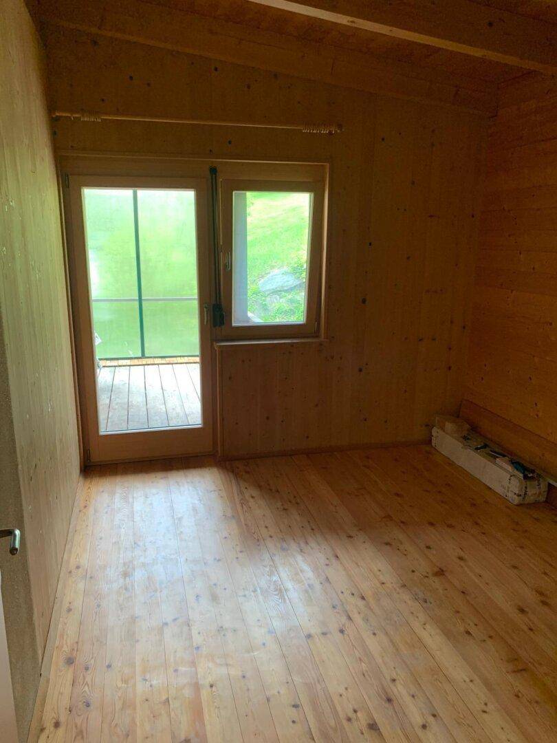 Leeres Zimmer mit Holzboden und Holzwänden, bietet Zugang zu einem Balkon.