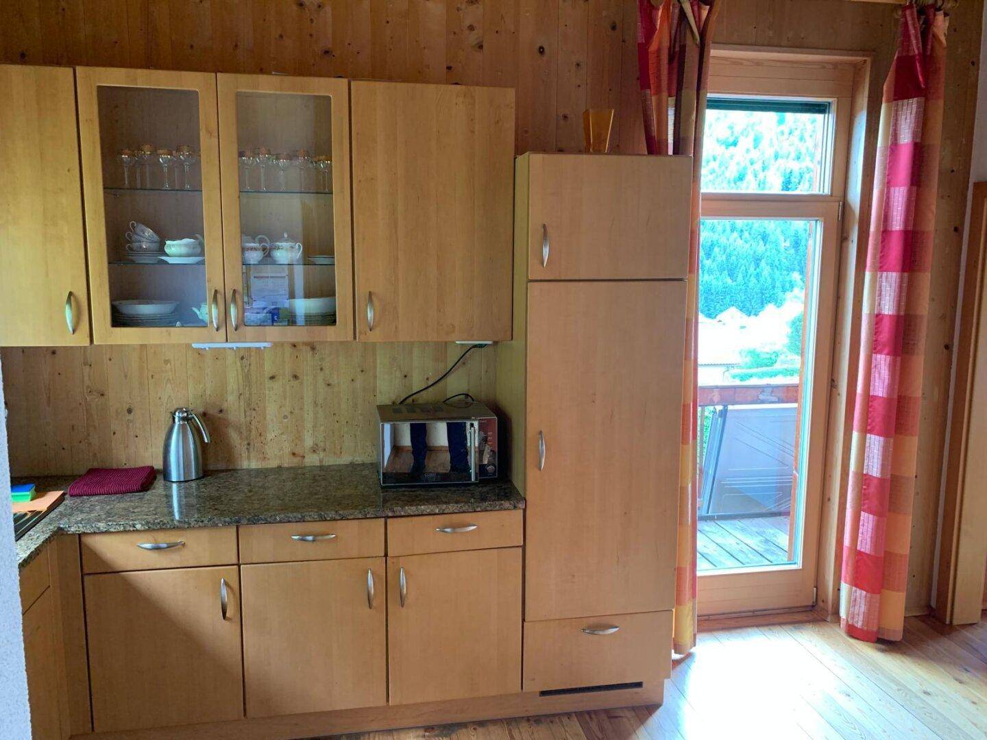 Küche mit Holzschränken, Granitarbeitsplatte und Fenster mit Blick ins Grüne.