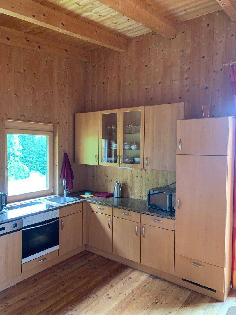 Küchenzeile mit Spüle, Kochfeld und weiteren Holzschränken, gut beleuchtet durch das Fenster.