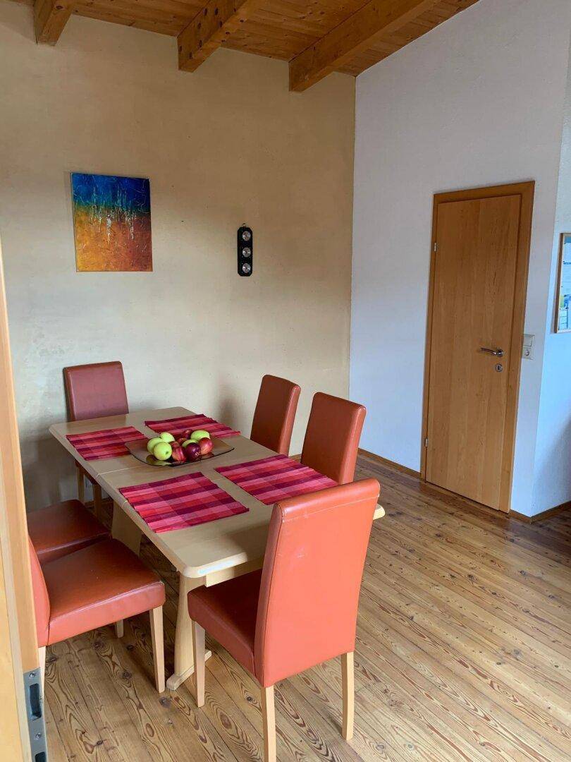 Essbereich mit Holztisch und orangefarbenen Stühlen auf einem Holzboden.