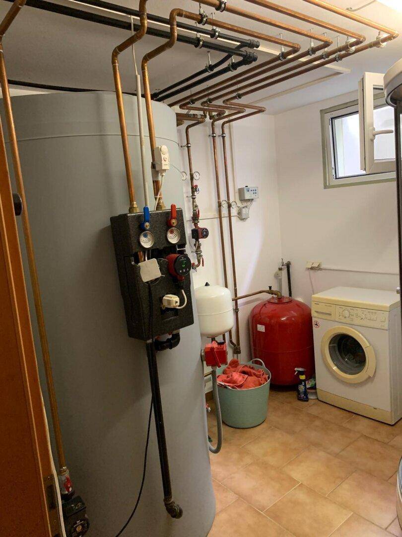 Hauswirtschaftsraum mit Warmwasserspeicher, Waschmaschine und Fliesenboden.