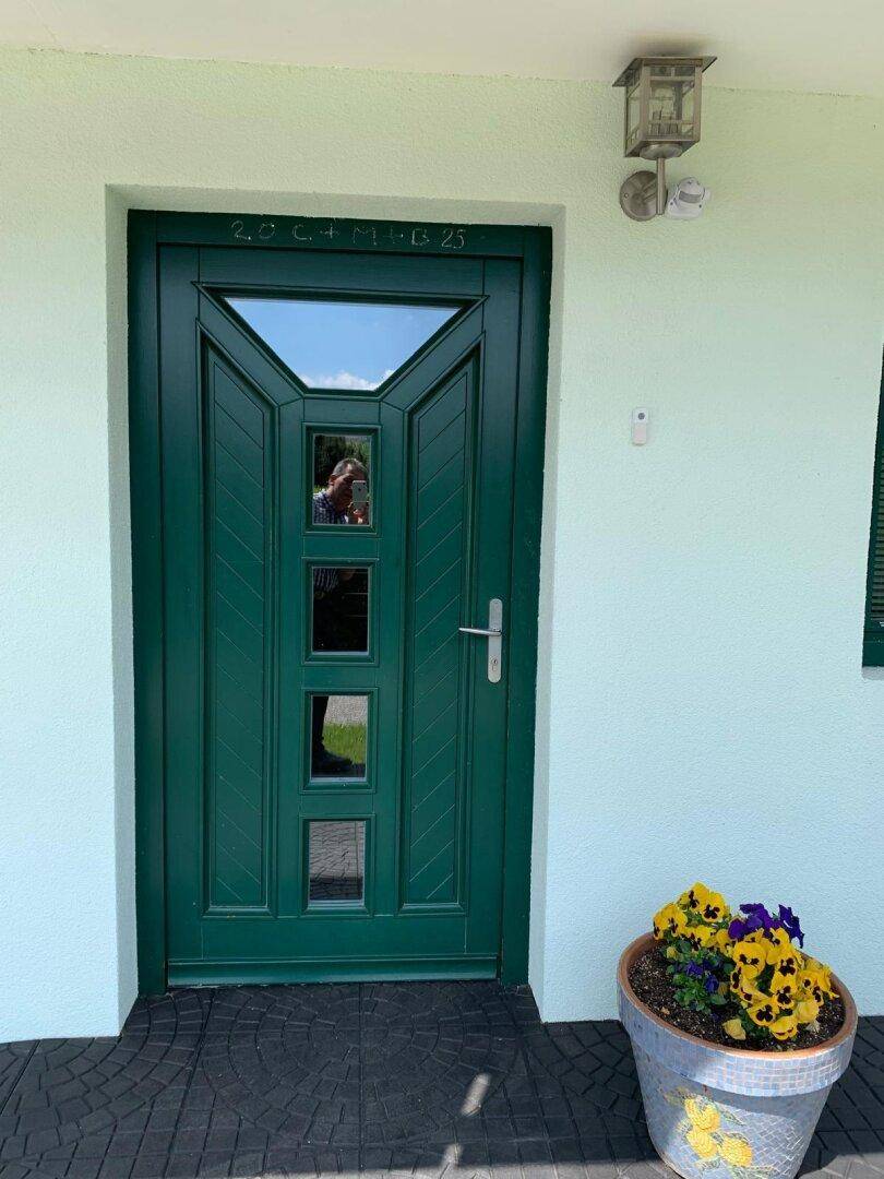 Grüne Eingangstür mit dekorativem Blumenkübel, einladend gestaltet.