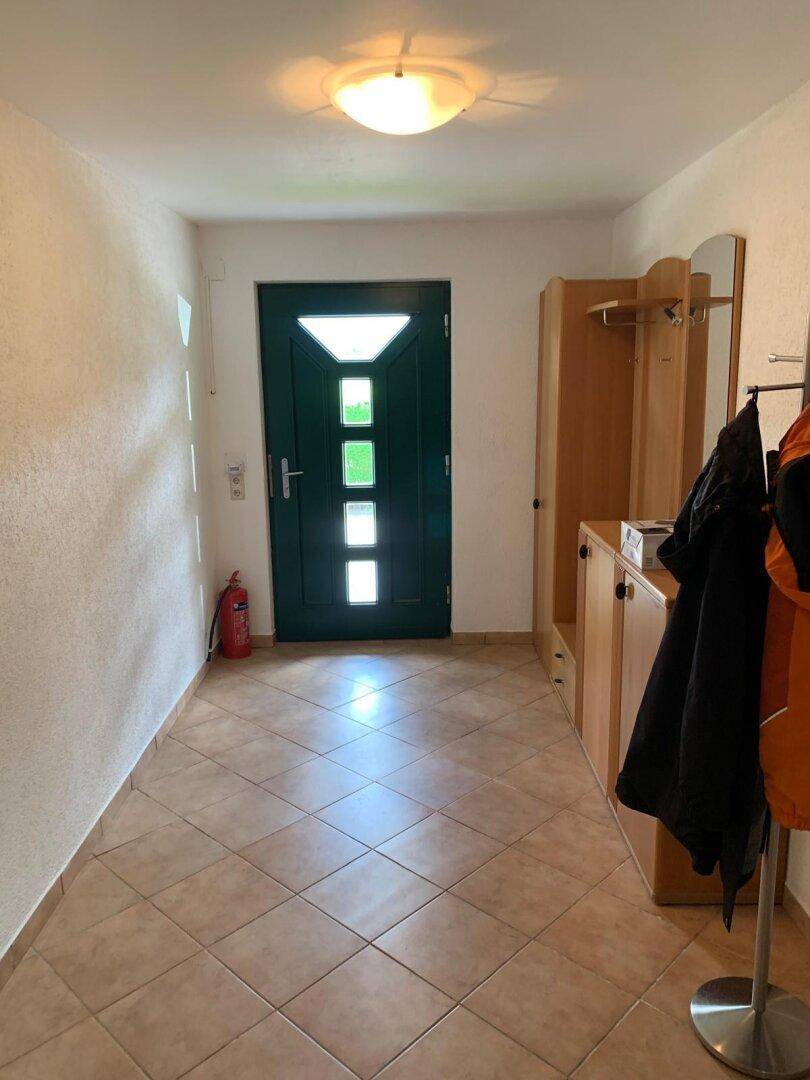 Eingangsbereich mit Fliesenboden, dunkler Haustür und praktischen Holzmöbeln.