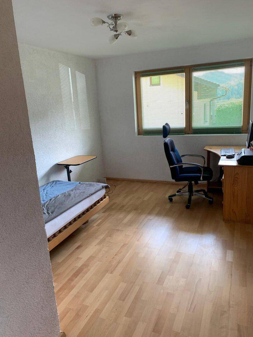Helles Schlafzimmer mit Holzboden, Schreibtisch und Blick ins Grüne durch das Fenster.