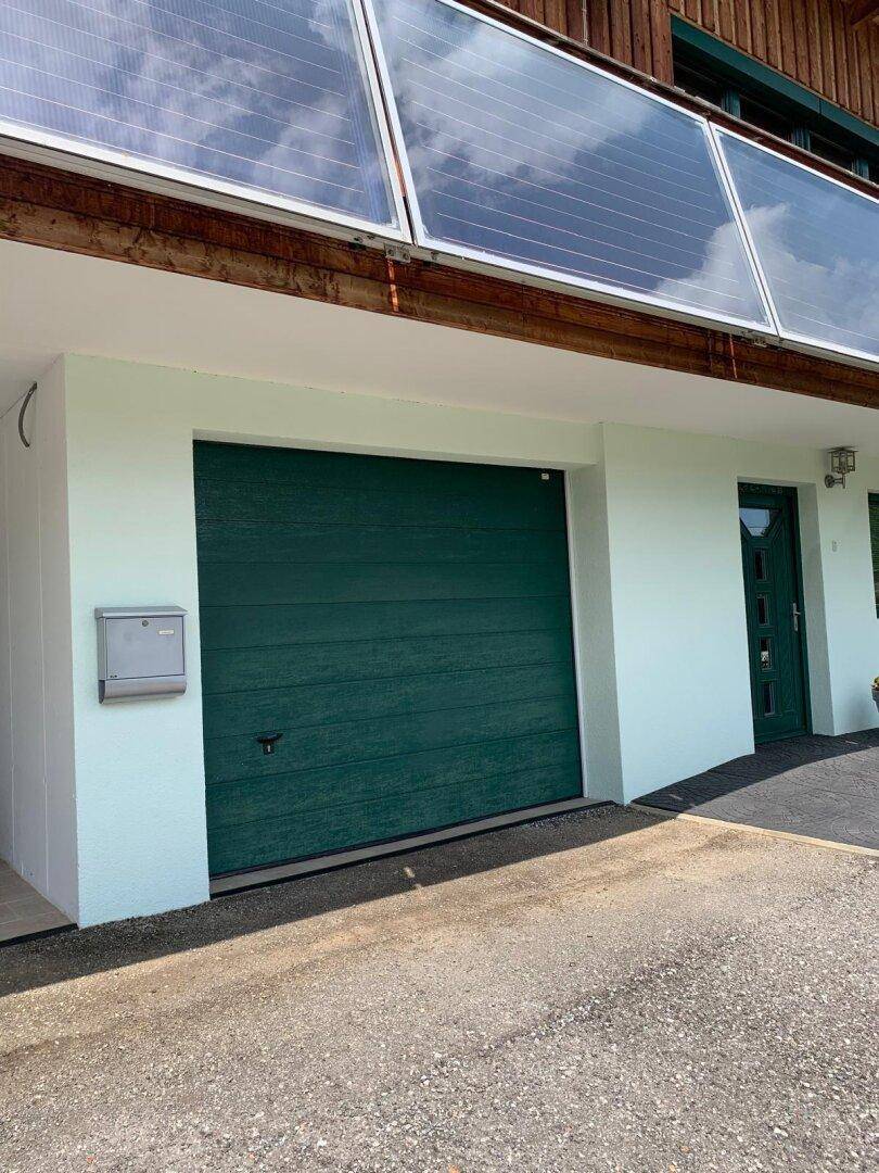 Grüne Garagentür und Eingangsbereich des Hauses mit heller Fassade.