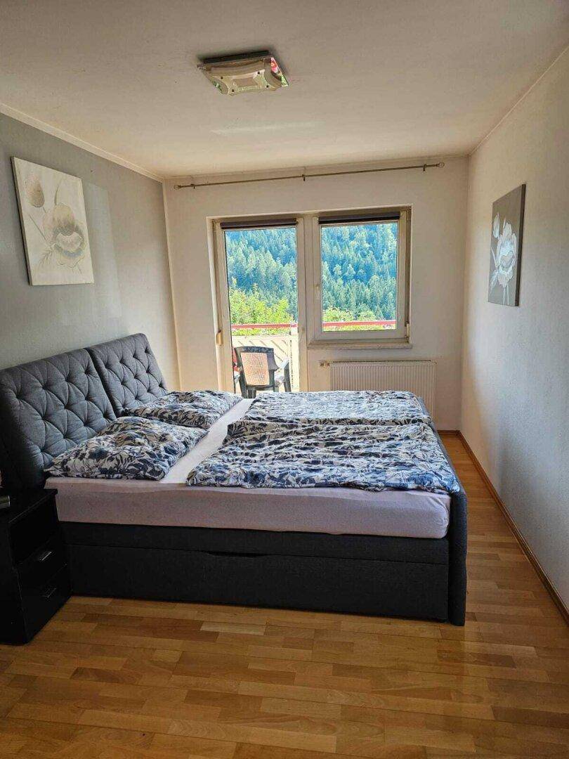 Gemütliches Schlafzimmer mit großem Bett, Holzboden und Fenster mit Blick auf die grüne Landschaft.