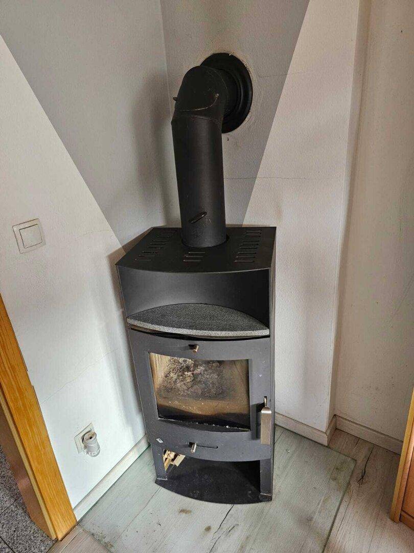 Moderner Holzofen in einer Ecke mit schwarzem Ofenrohr, bereit für gemütliche Wärme.