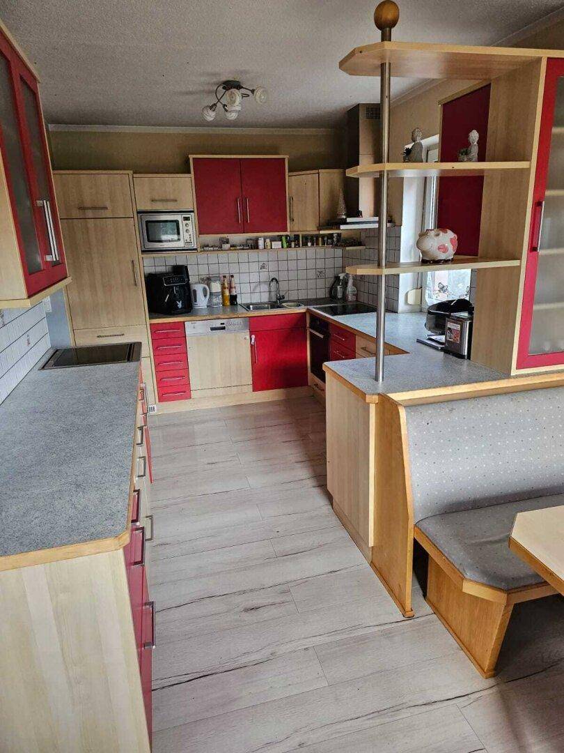 Küche mit Holzschränken, roten Akzenten und einer gemütlichen Essecke mit integrierter Sitzbank.
