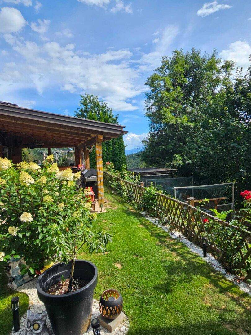 Gepflegter Gartenweg mit üppiger Bepflanzung, Holzpergola und malerischem Bergblick in der Ferne.