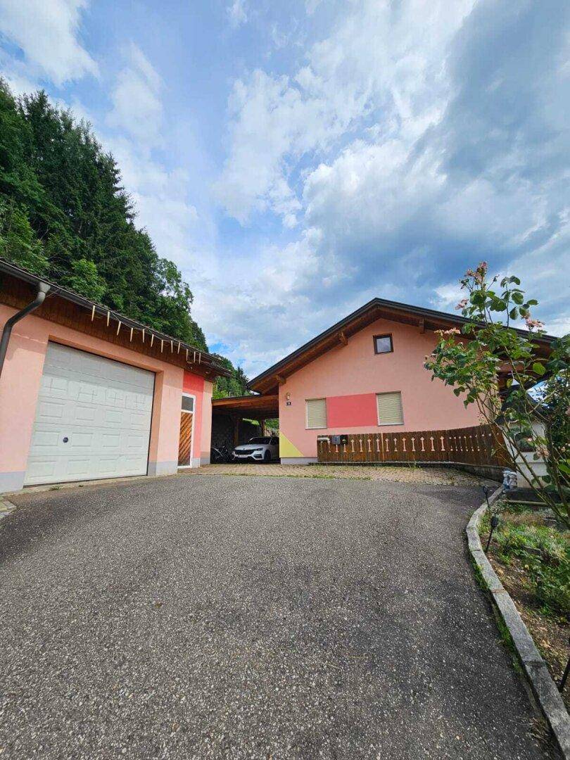 Außenansicht des Hauses mit Garage, Carport und Zufahrt, umgeben von grüner Landschaft.