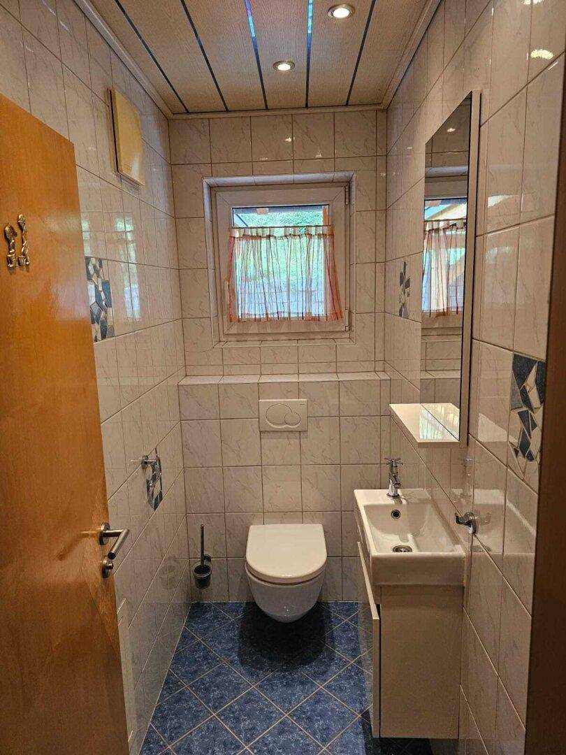 Kleines Gäste-WC mit blauen Bodenfliesen, wandhängender Toilette und kleinem Waschbecken.