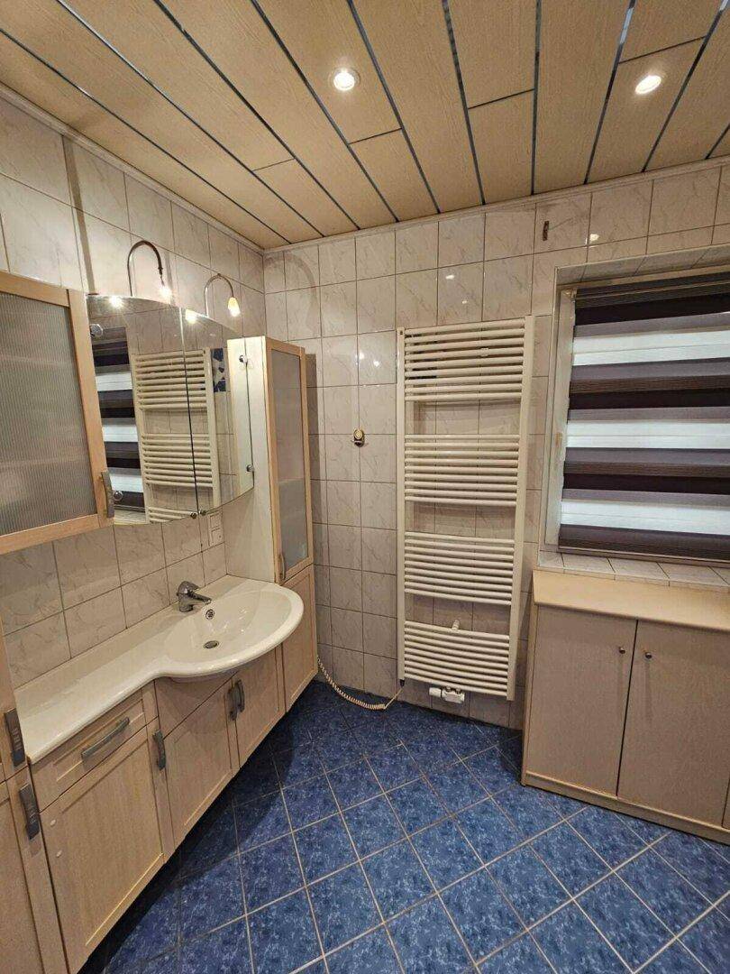 Badezimmer mit blauen Bodenfliesen, weiß gefliesten Wänden, Waschtisch und beheiztem Handtuchhalter.