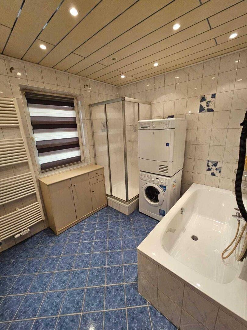 Badezimmer mit blauen Fliesen, Duschkabine, Badewanne, beheiztem Handtuchhalter und Waschmaschine.
