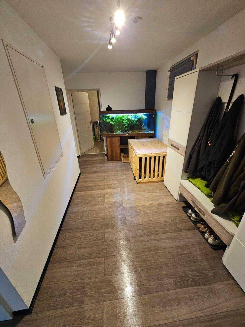 Geräumiger Flur mit Holzfußboden, Garderobe, Schuhablage und einem großen Aquarium als Blickfang.