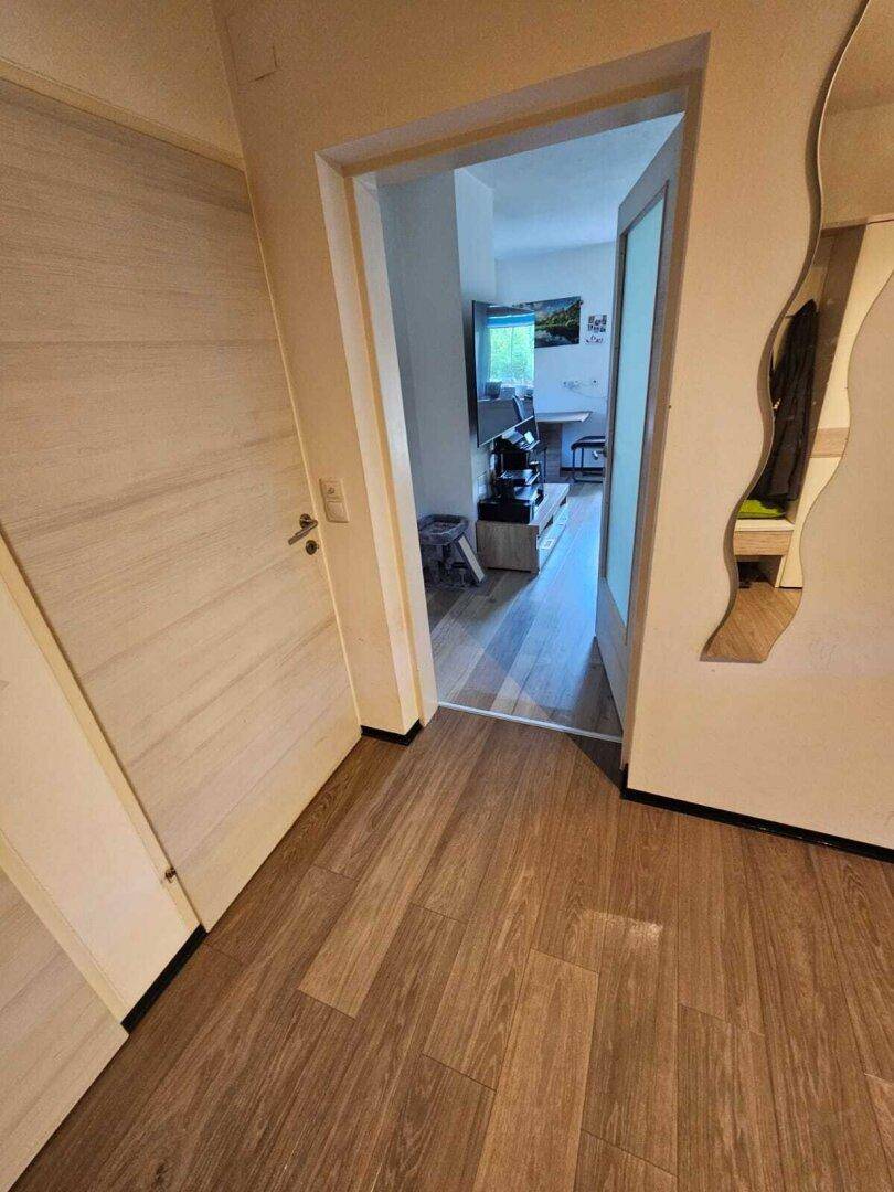 Heller Flur mit Laminatboden, modernem Wellenspiegel und Zugang zu einem angrenzenden Raum.