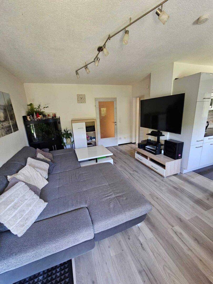 Geräumiges Wohnzimmer mit großem grauen Ecksofa, Fernseher und hellem Laminatboden.