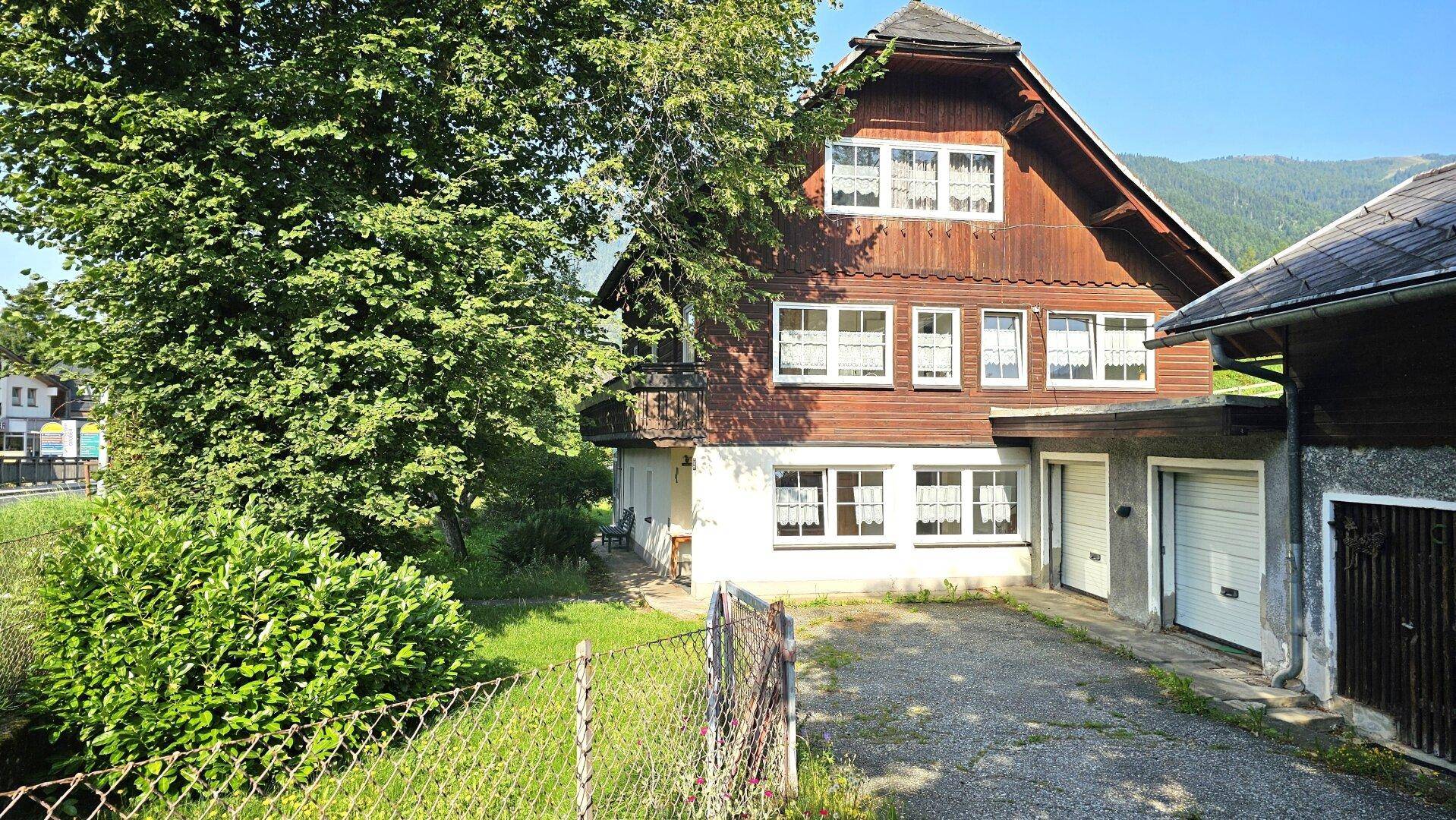Charmantes Holzhaus mit weiß gerahmten Fenstern und Garagen, eingebettet in eine grüne Landschaft.