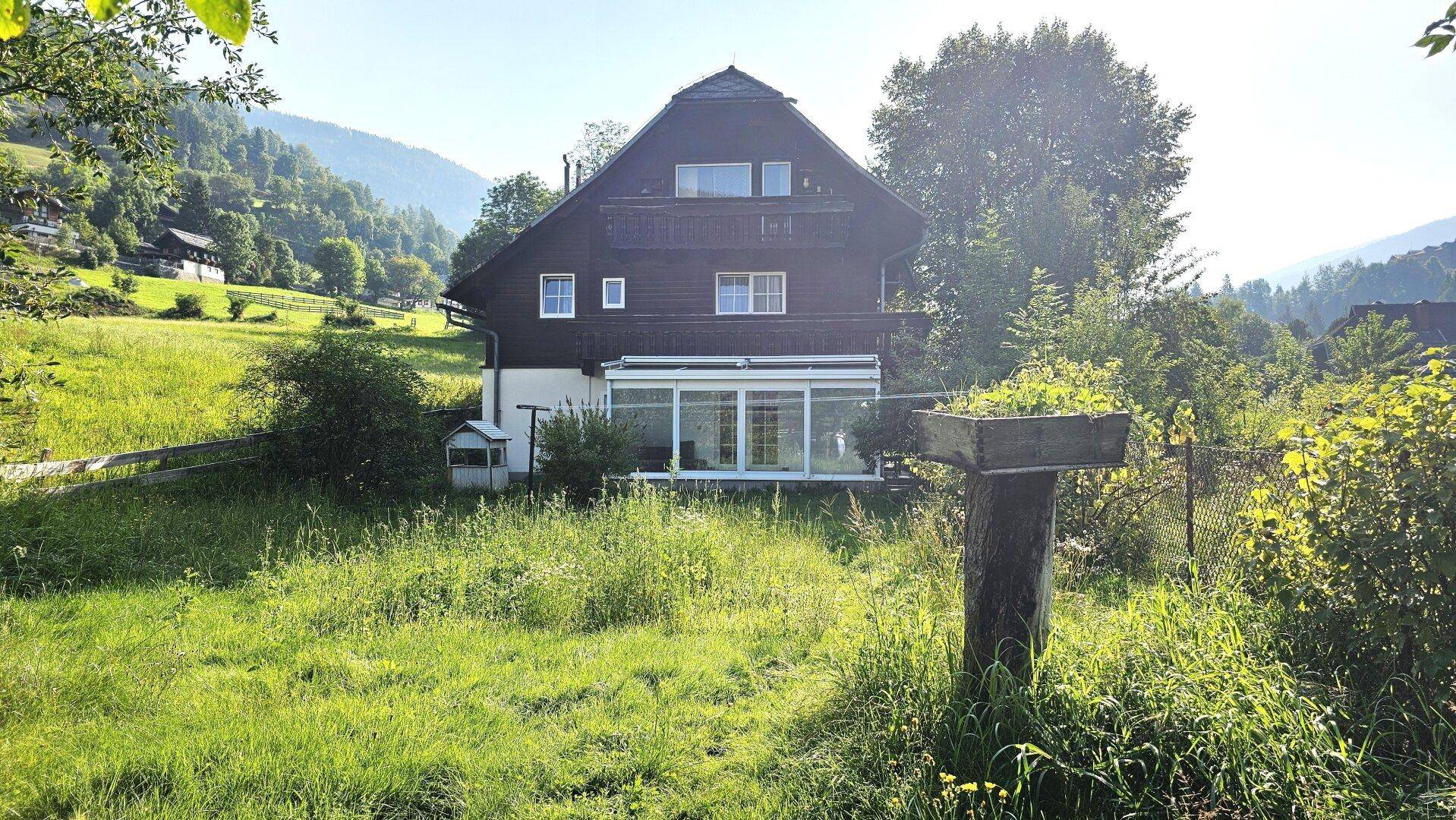 Rückseite des Hauses mit einem Wintergarten und einer weitläufigen, grünen Gartenfläche.