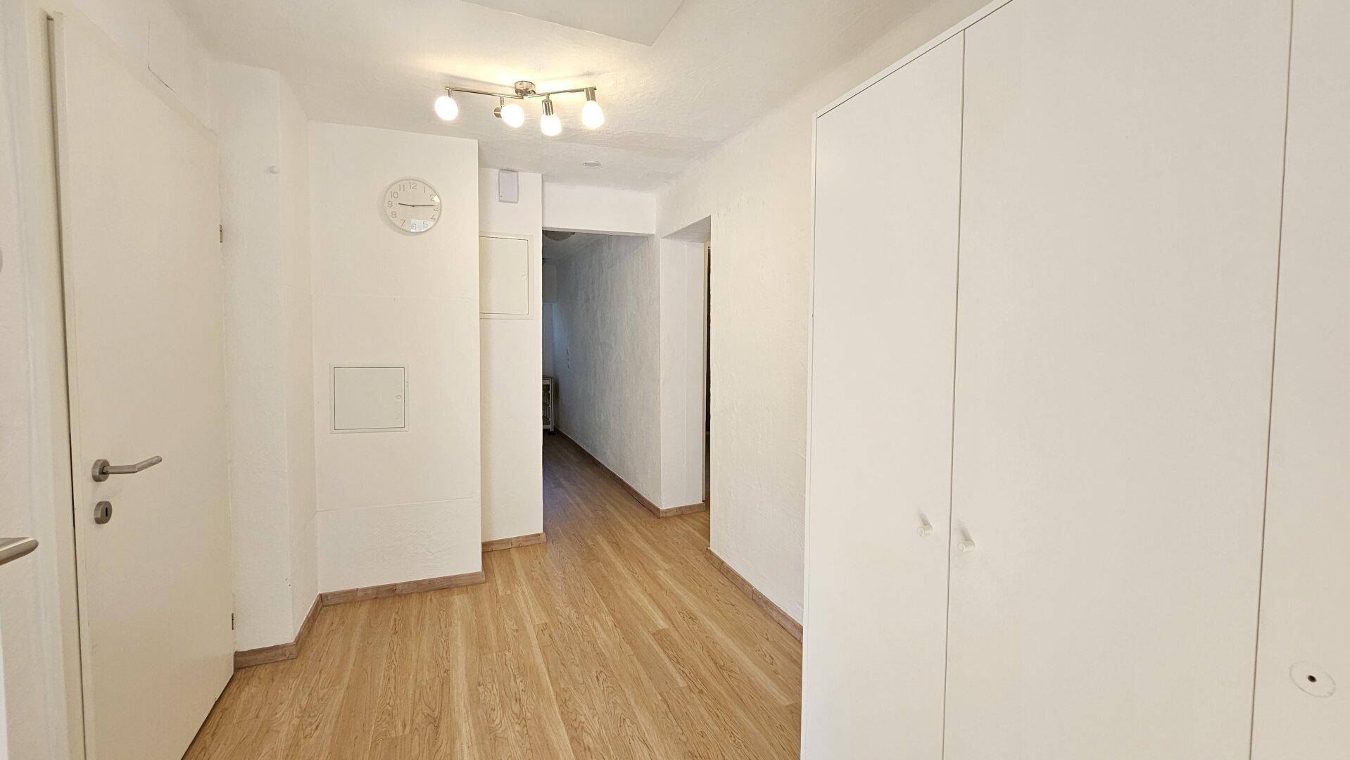 Heller Flur mit modernem Laminatboden und weißen Einbauschränken, der zu weiteren Räumen führt.