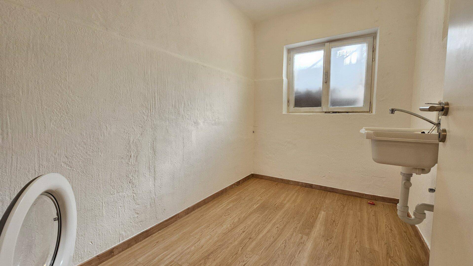 Kleines WC mit Fenster, Waschbecken und hellem Laminatboden, funktional und sauber.