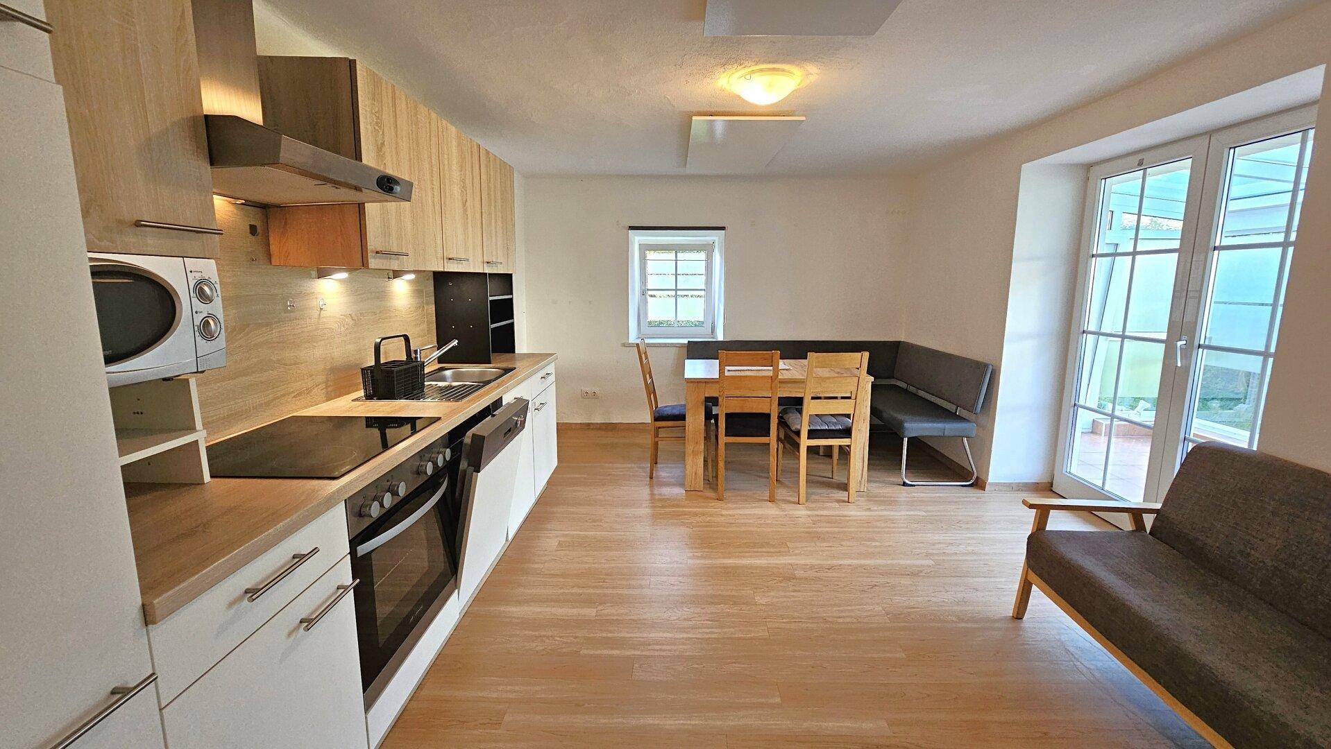 Offene Küche mit Essbereich, modernen Holzfronten, Laminatboden und Zugang zu einem Balkon.