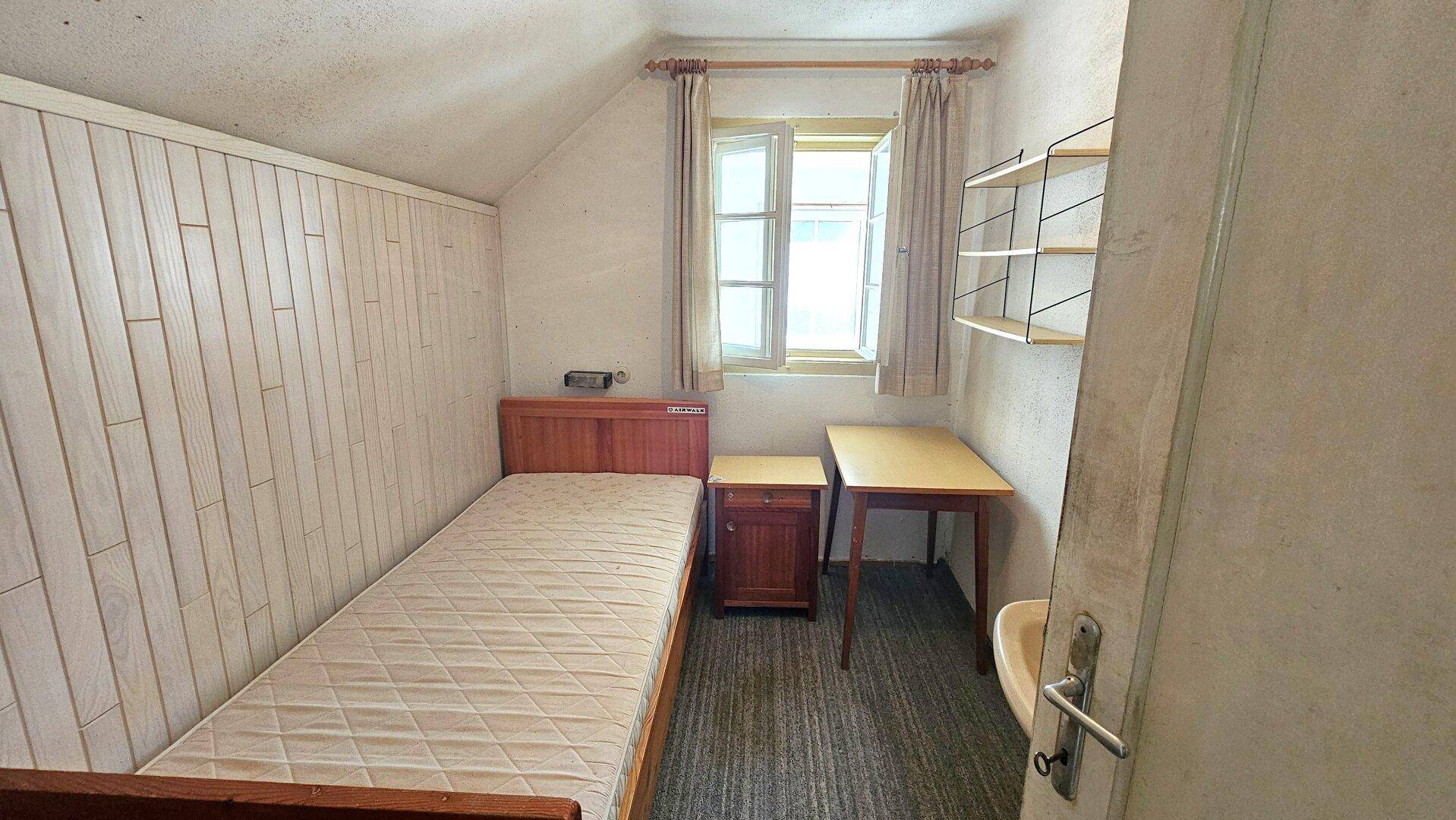 Kleines Schlafzimmer mit Einzelbett, Holzvertäfelung und Schreibtisch, ideal als Gästezimmer.