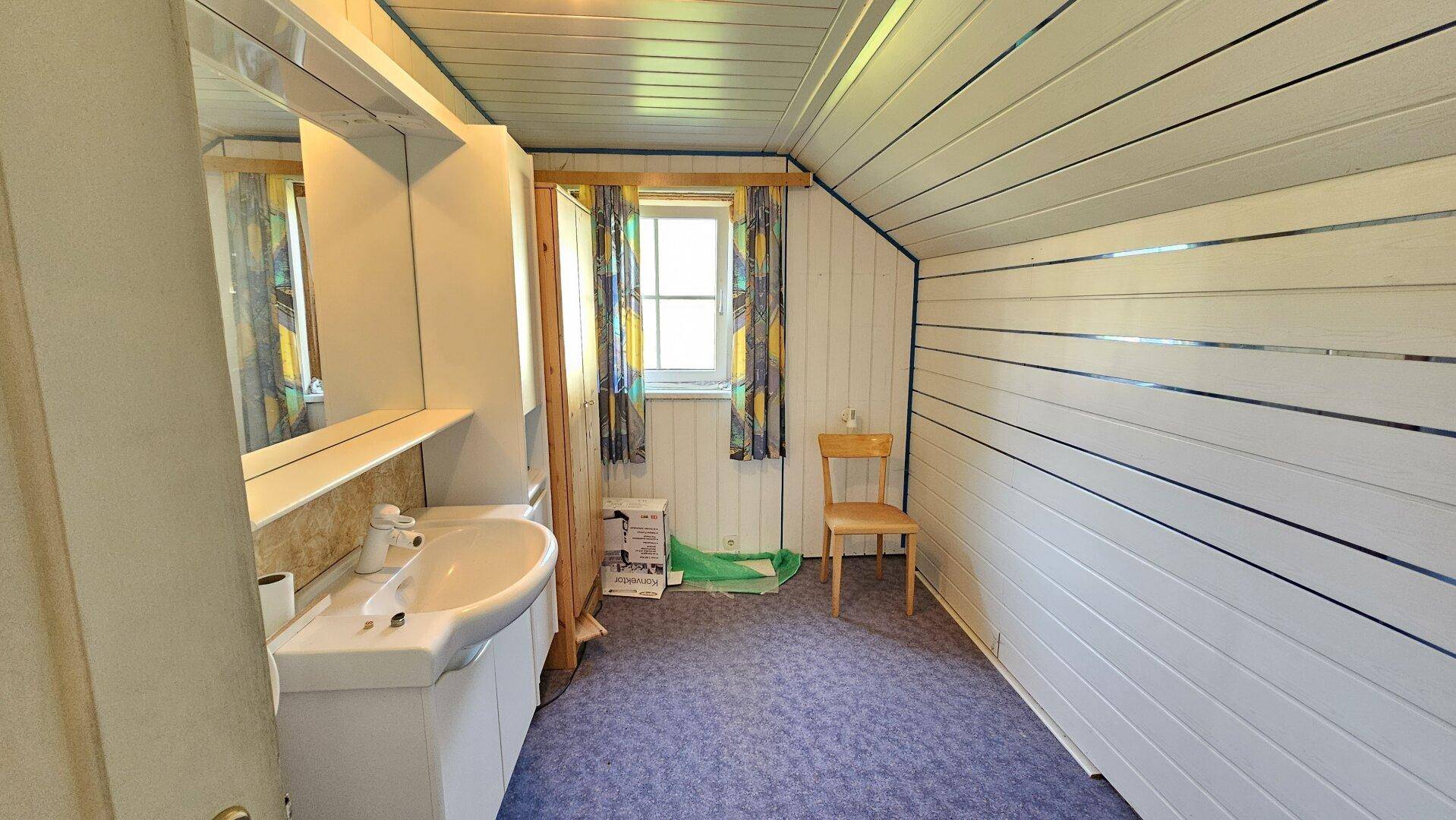 Badezimmer im Dachgeschoss mit Waschtisch, Spiegelschrank und Holzvertäfelung, mit Fenster.
