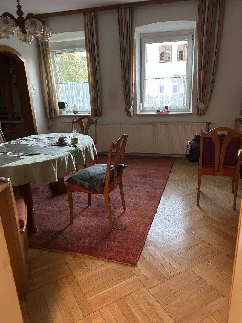 Essbereich mit Holztisch, Stühlen und Parkettboden neben einem Fenster.