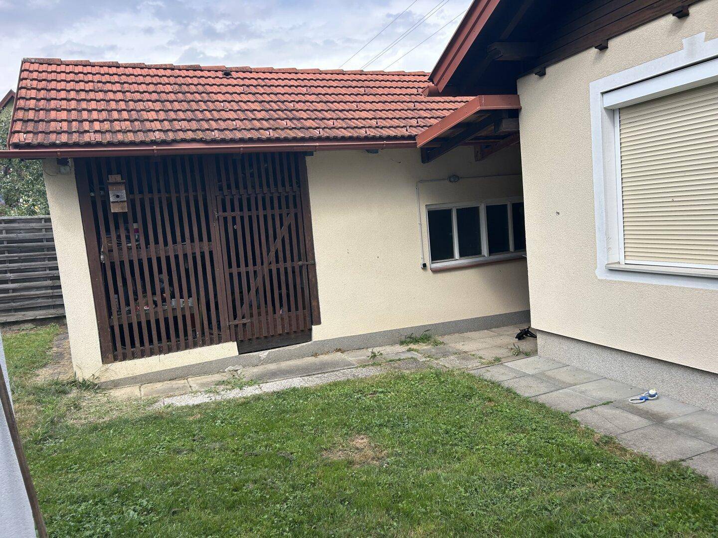 Seitenansicht des Hauses mit einem kleinen Nebengebäude und Rasenfläche.